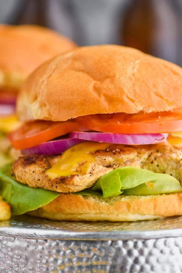 close up of a grilled chicken sandwich with lettuce on the bottom, then the chicken breast, then honey bbq sauce, then red onions and tomatoes