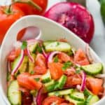 white bowl full of cucumber tomato salad topped with fresh parsley