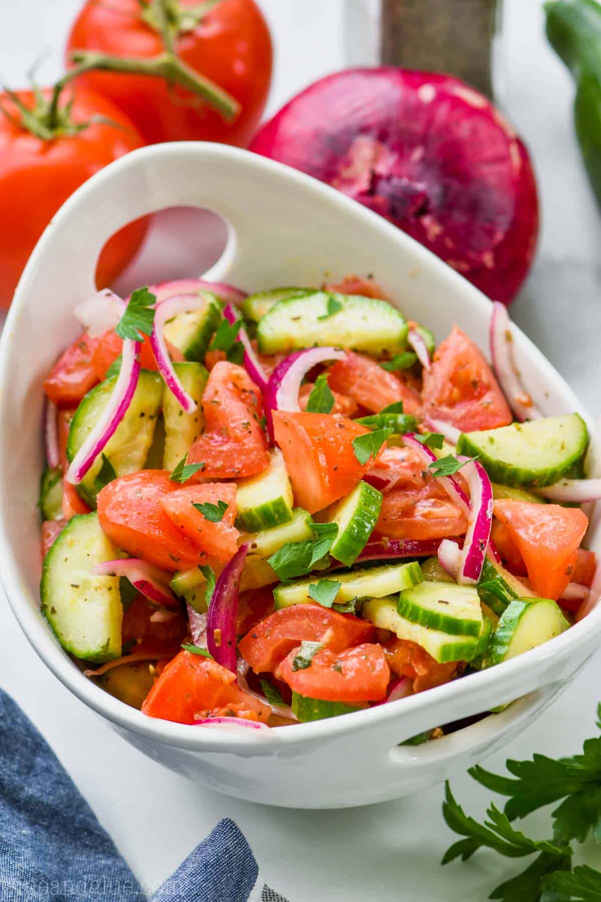 white bowl full of cucumber tomato salad topped with fresh parsley