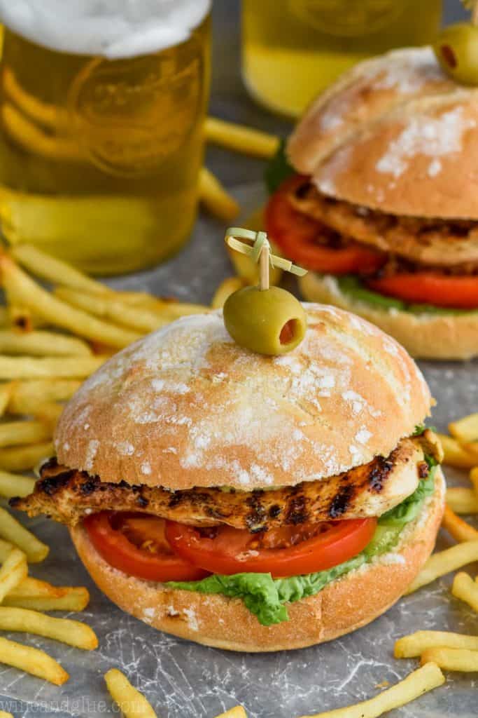 grilled chicken sandwich recipe on a bun with an olive and toothpick and fries around it