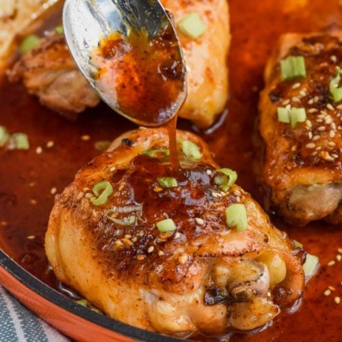 spooning honey garlic sauce over baked chicken thighs in a pan