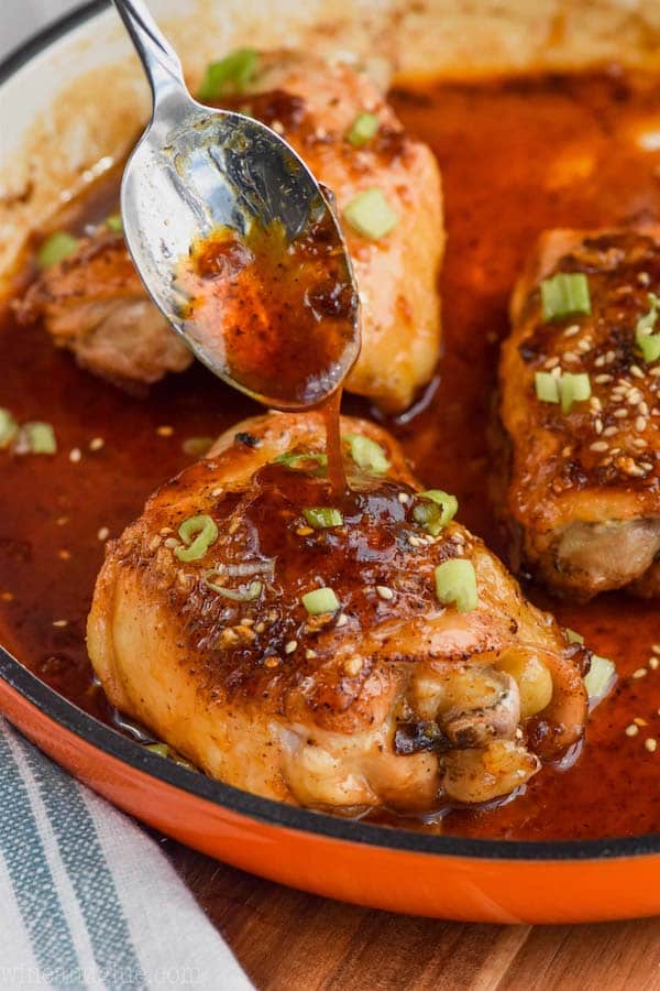 spooning honey garlic sauce over baked chicken thighs in a pan