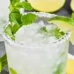 small tumbler glass filled with mojito margarita recipe with salt rim, lime wedge, and mint sprig