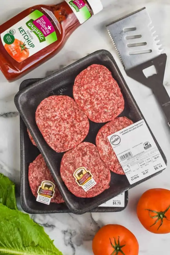 picture of hamburger meat in their packaging surrounded by lettuce, tomatoes, ketchup, and a spatula