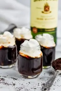 four shots of irish coffee topped with whipped cream