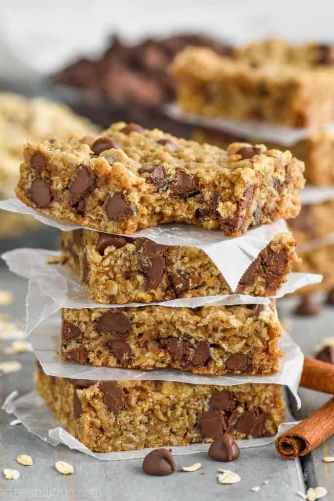 A stack of four Oatmeal Chocolate Chip Bars with square parchment paper pieces underneath each one. This most top bar on the stack has a small bite. 