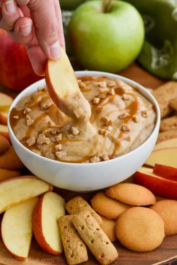 an apple being dipped into cream cheese caramel apple dip