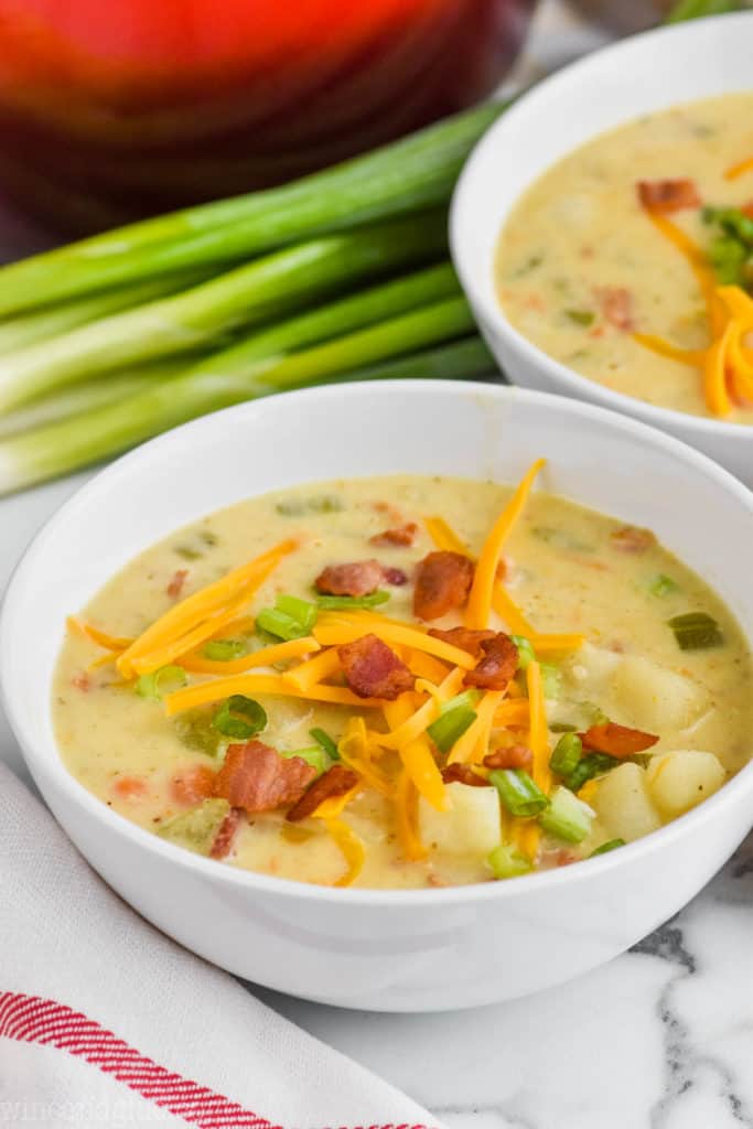 bowl of creamy potato soup with bacon topped with cheese, bacon, and scallions