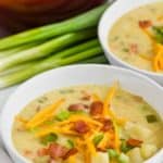 bowl of creamy potato soup with bacon topped with cheese, bacon, and scallions