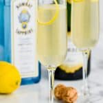 tall champagne flute filled with french 75 recipe , another champagne flue int he background, a bottle of champagne, a cork and a bottle bombay sapphire