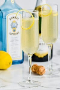 tall champagne flute filled with french 75 recipe , another champagne flue int he background, a bottle of champagne, a cork and a bottle bombay sapphire