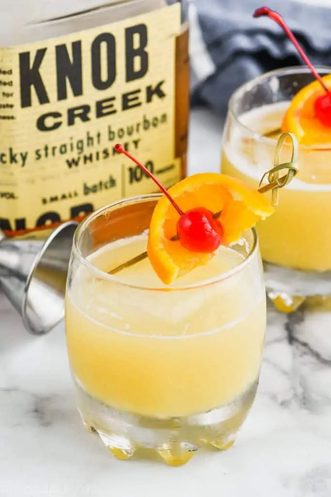 frothy glass of the best whiskey sour recipe garnished with an orange and cherry