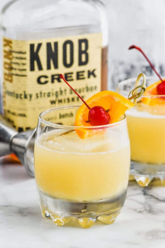 two whiskey sours in front of a bottle of knob creek