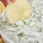 a hand dipping a chip into dill dip