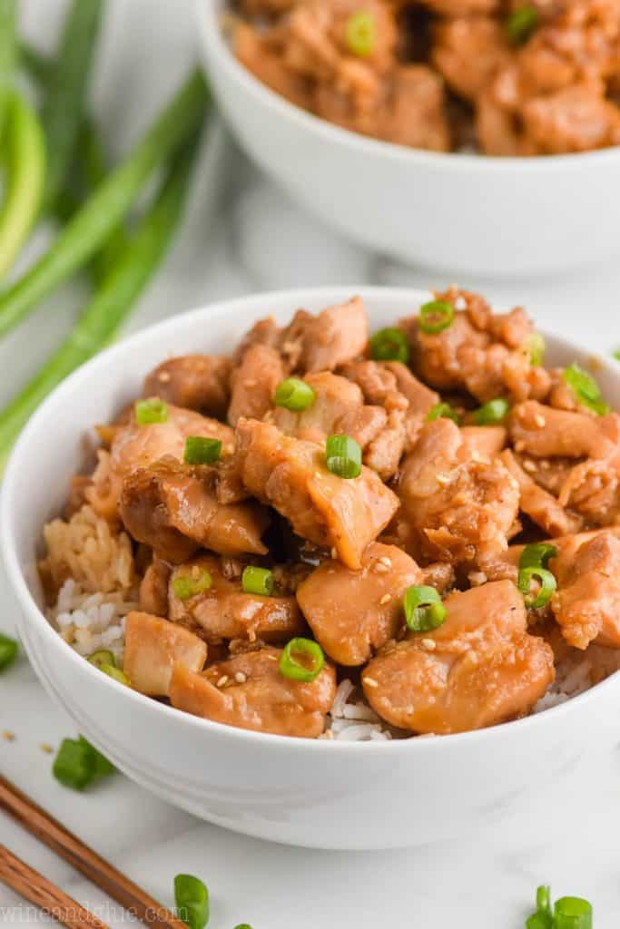 In a white bowl, white rice is topped with the Bourbon Chicken and sliced scallions