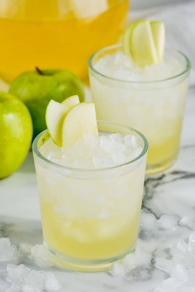 two cups of caramel apple vodka punch garnished with sliced apples