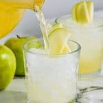 caramel apple vodka punch being poured into a glass of ice garnished with sliced apples - 14