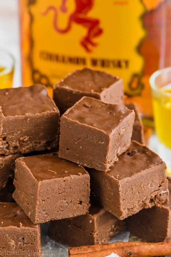 A pyramid stack of cubed Fireball Fudge with a cinnamon stick in the front and a bottle of Fireball in the back