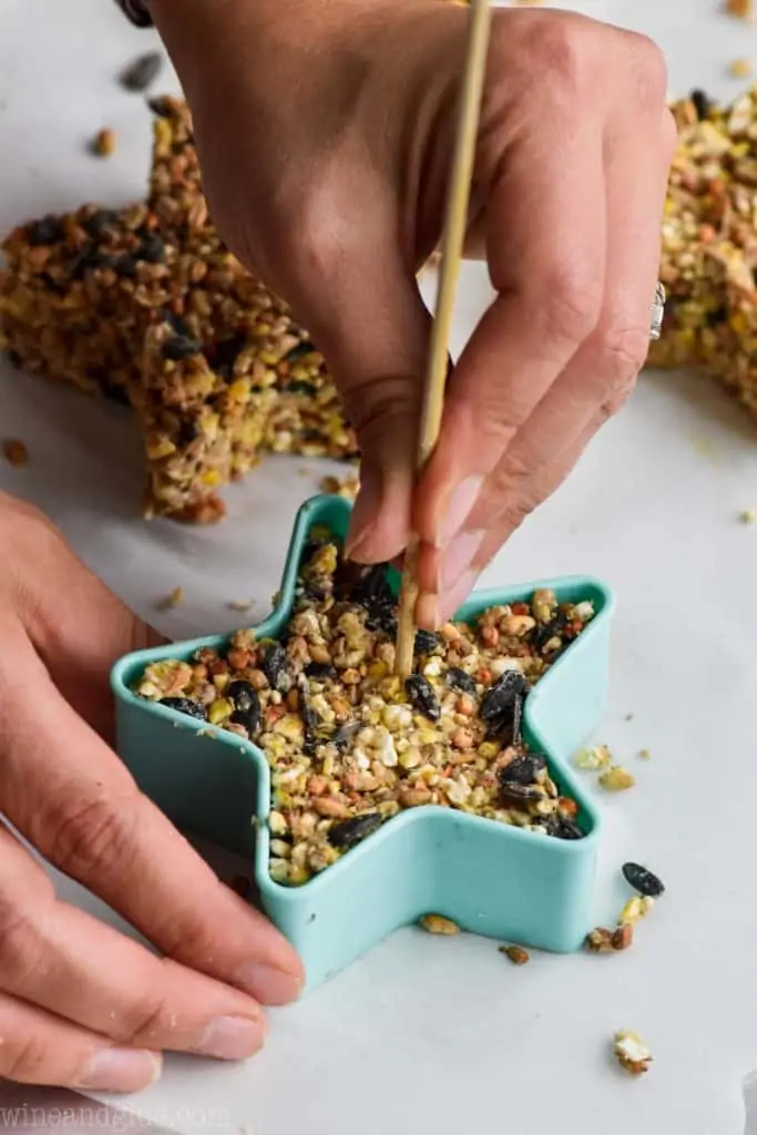 In a star shaped cookie mold, some of the bird feeder mixture is inside while having a hole created with a skewer