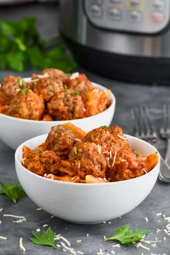 two bowls of instant pot meatballs and pasta garnished with parsley and cheese