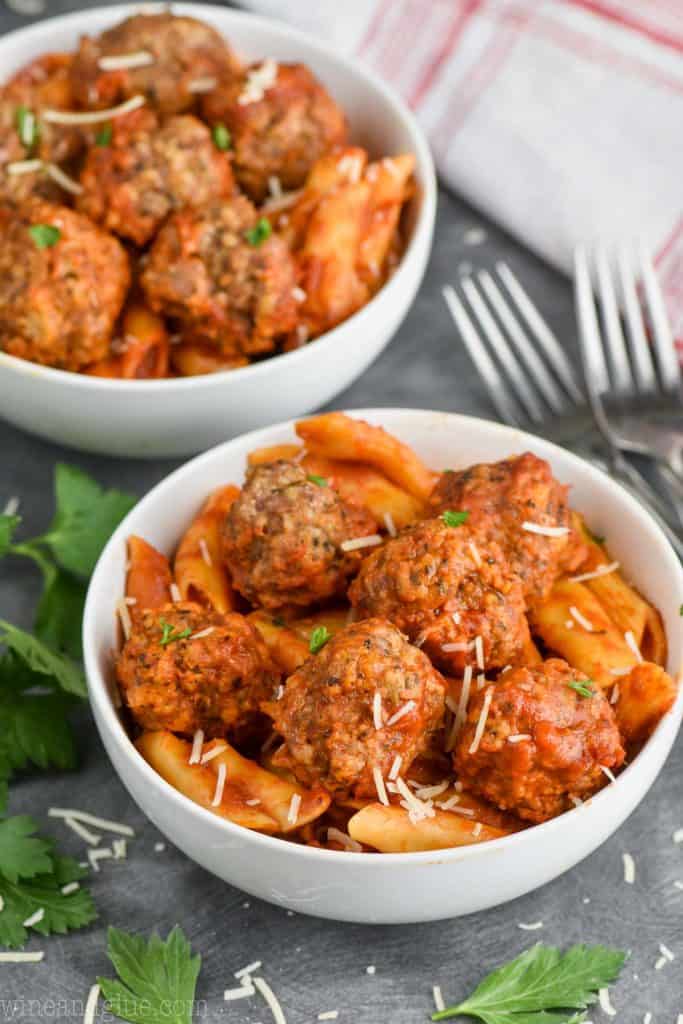 bowl of instant pot meatballs and pasta garnished with parsley and shredded cheese. 