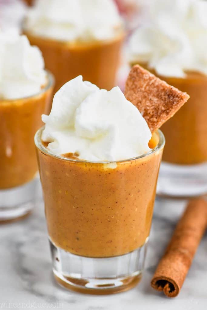 shot glass full of pumpkin pie shot topped with whipped cream and a slice of pie crust