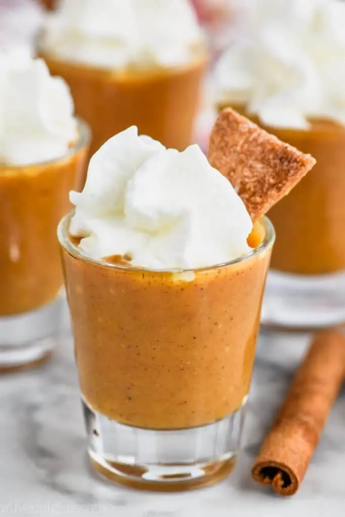 shot glass full of pumpkin pie shot topped with whipped cream and a slice of pie crust