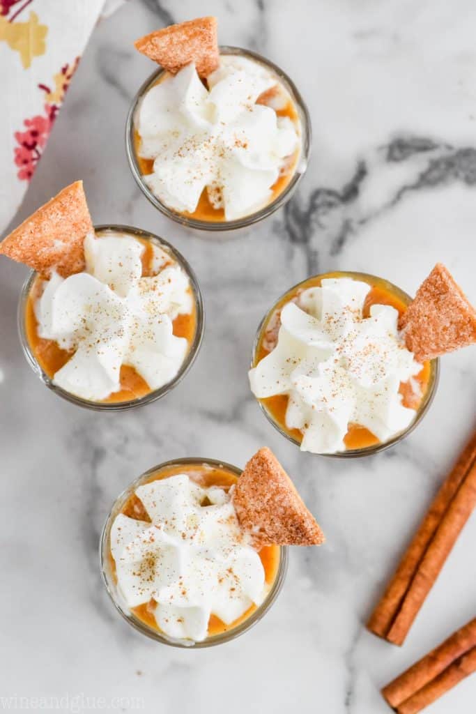 overhead view of pumpkin pudding shots that are topped with whip cream, cinnamon, and pie crust