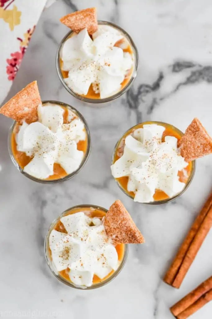 overhead view of pumpkin pudding shots that are topped with whip cream, cinnamon, and pie crust