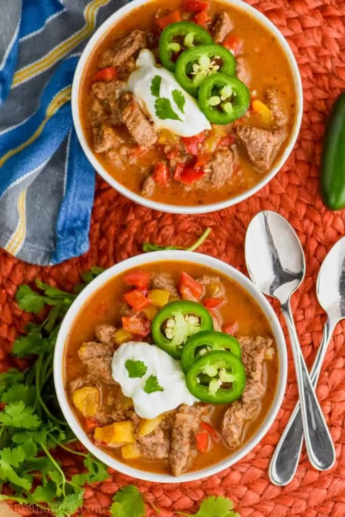 two bowls of steak fajita soup garnished with sour cream, jalapeños and cilantro