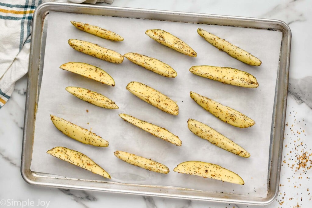 cut potatoes that have been seasoned on a rimmed baking sheet ready to be baked