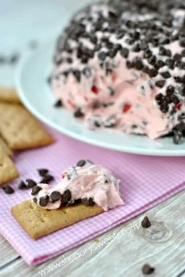 The Cherry Chocolate Chip Cheese Ball is in the background, and in the foreground, a graham cracker has some of the cheese ball on it  