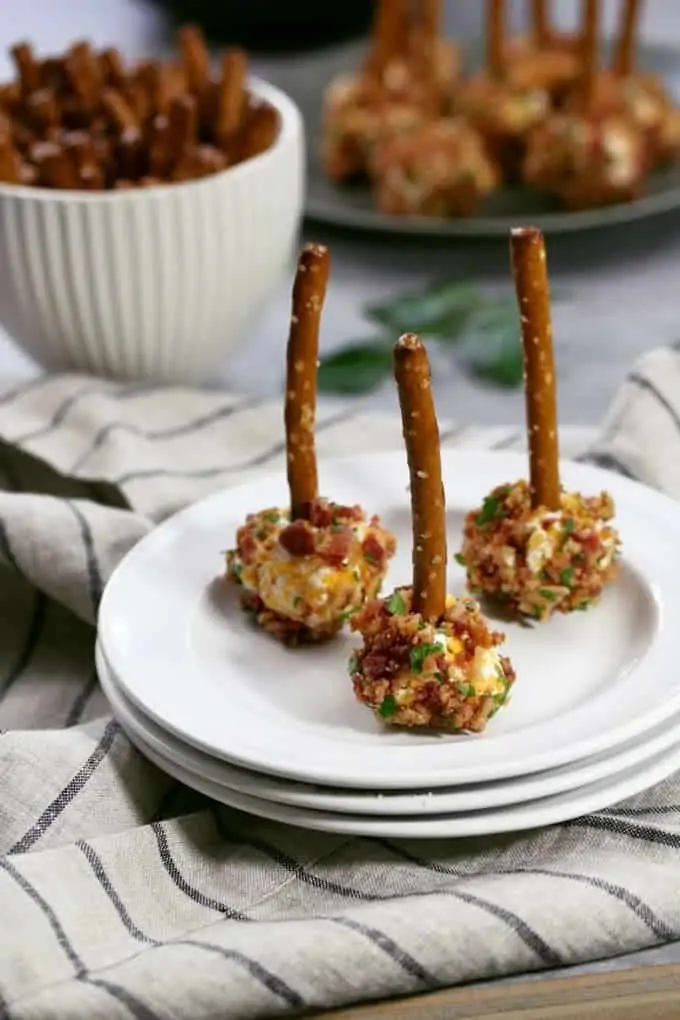In the middle of a white plate, there are three Mini Bacon Ranch Cheese Balls with stick pretzels in the middle of them.  