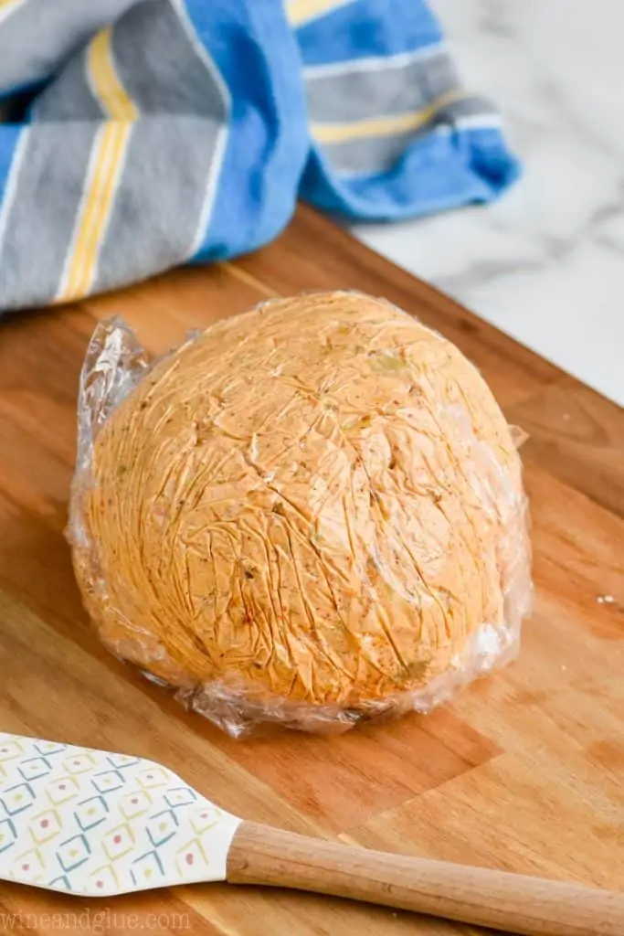 easy cheese ball recipe wrapped in saran wrap and formed into a ball