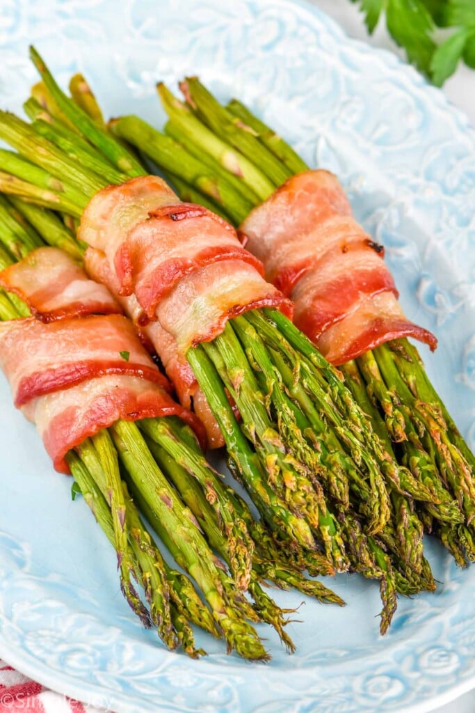 four bundles of asparagus wrapped in bacon on a platter