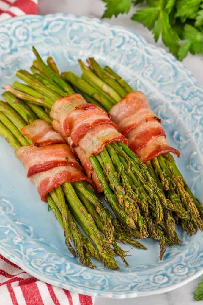 baked bacon wrapped asparagus, a great side dish on a blue platter