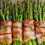 four groups of bacon wrapped asparagus baked with brown sugar on a tray