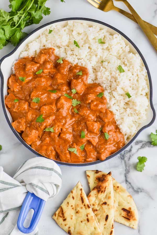 pan of creamy butter chicken with rice, cilantro and naan