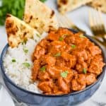 chicken butter masala recipe in a bowl with rice and naan