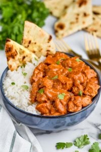 chicken butter masala recipe in a bowl with rice and naan