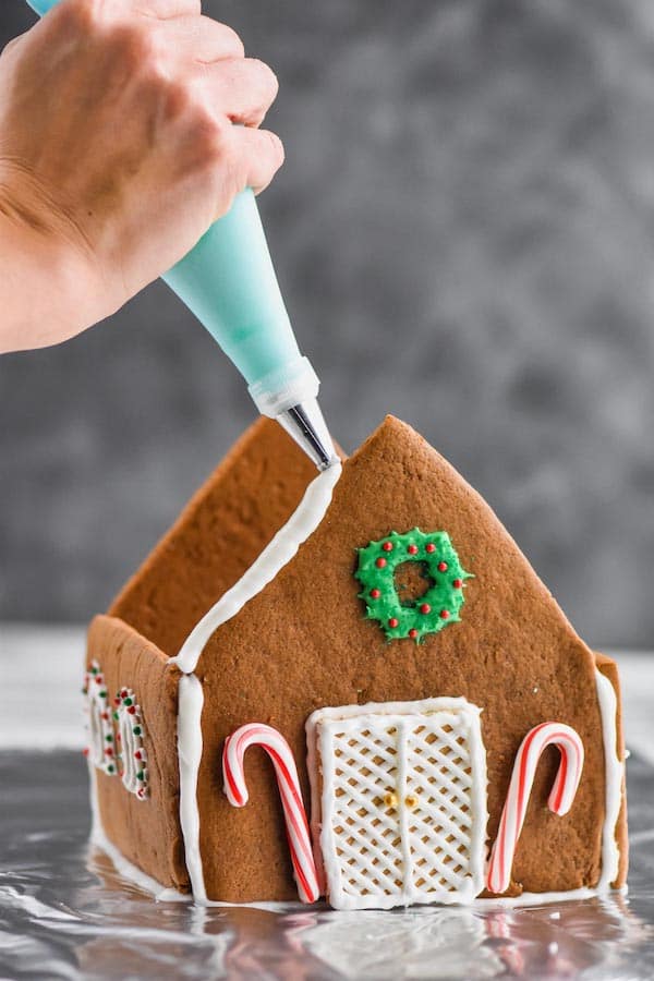 piping gingerbread icing on a built gingerbread house recipe