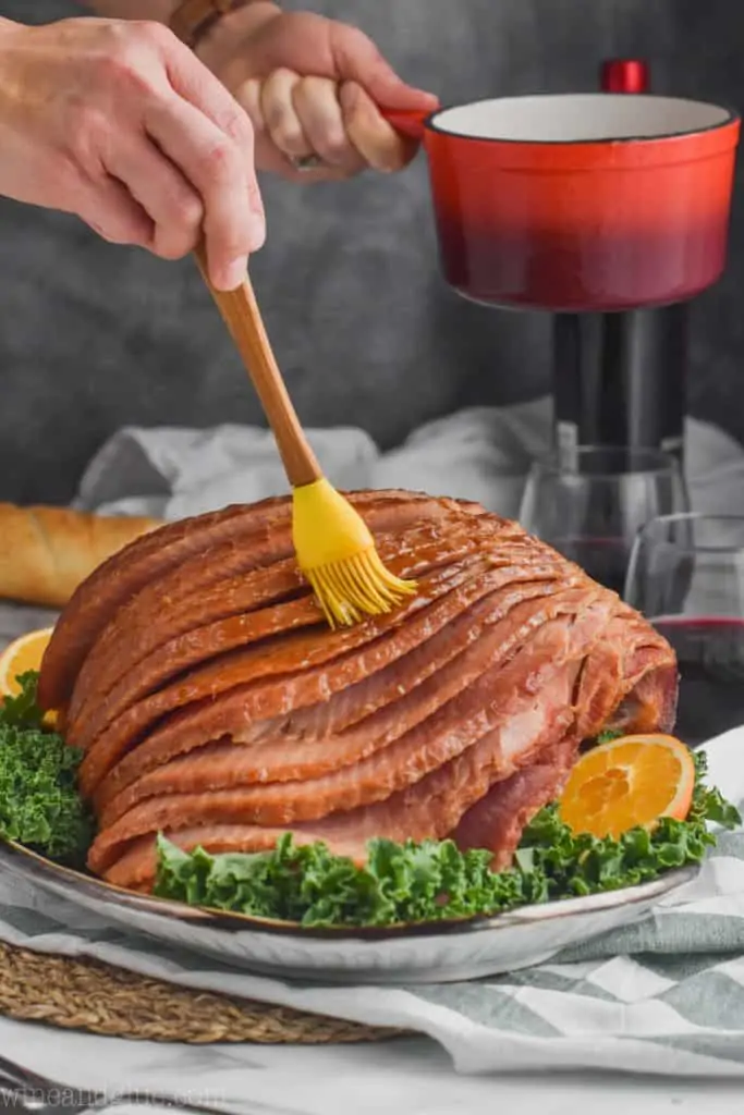 brushing more brown sugar glaze for ham onto a slow cooker spiral cut ham