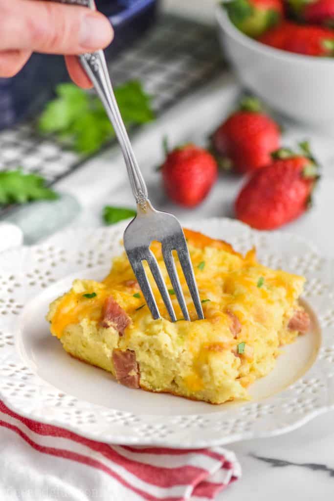 fork going into overnight ham and egg breakfast casserole on a white plate