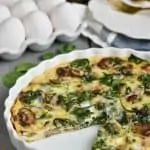 a spinach and mushroom quiche in a white quiche dish with a piece missing
