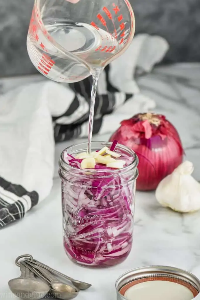 liquid being poured into a jar to make quick and easy pickled red onions