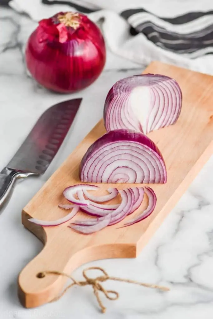 red onions being sliced as a julienne shape on a cutting board to show how to make pickled red onions