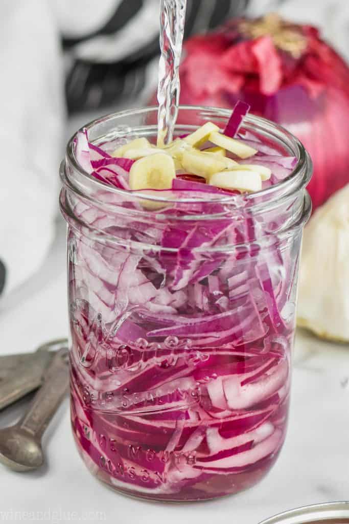 pouring liquid into a jar of sliced red onions to make quick pickled red onions