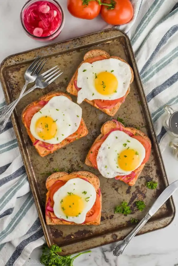 four pieces of toast with hummus and eggs on them on a baking sheet