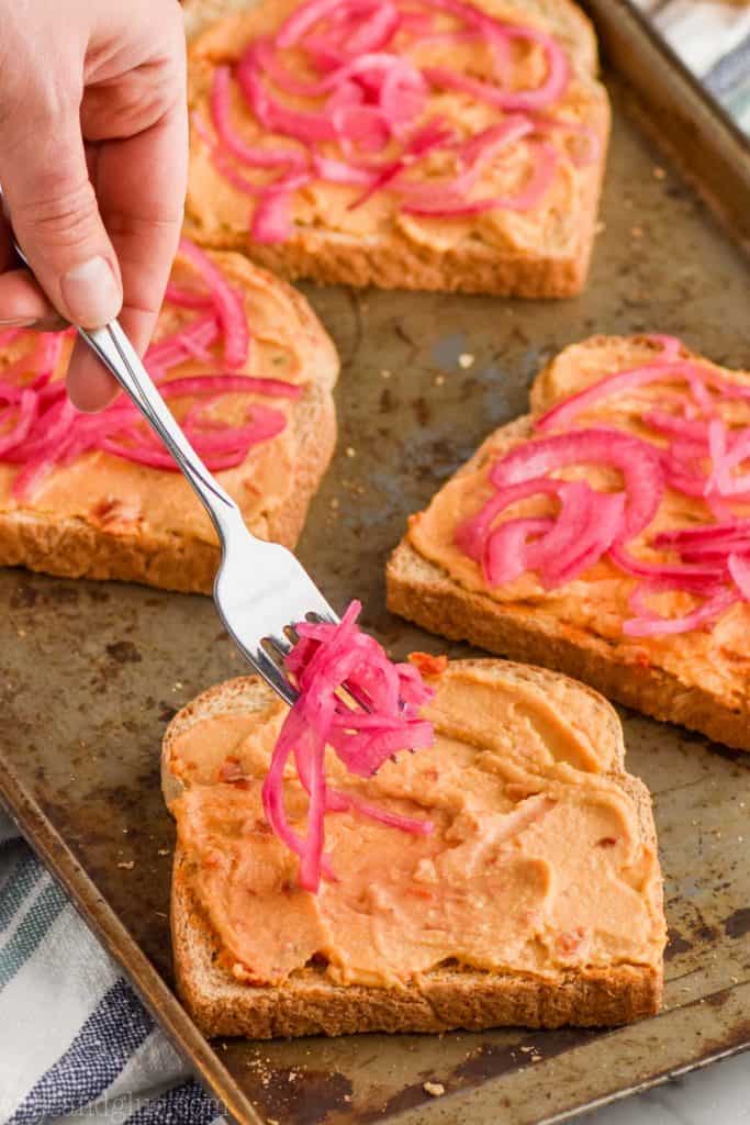 putting red pickled onions on hummus toast