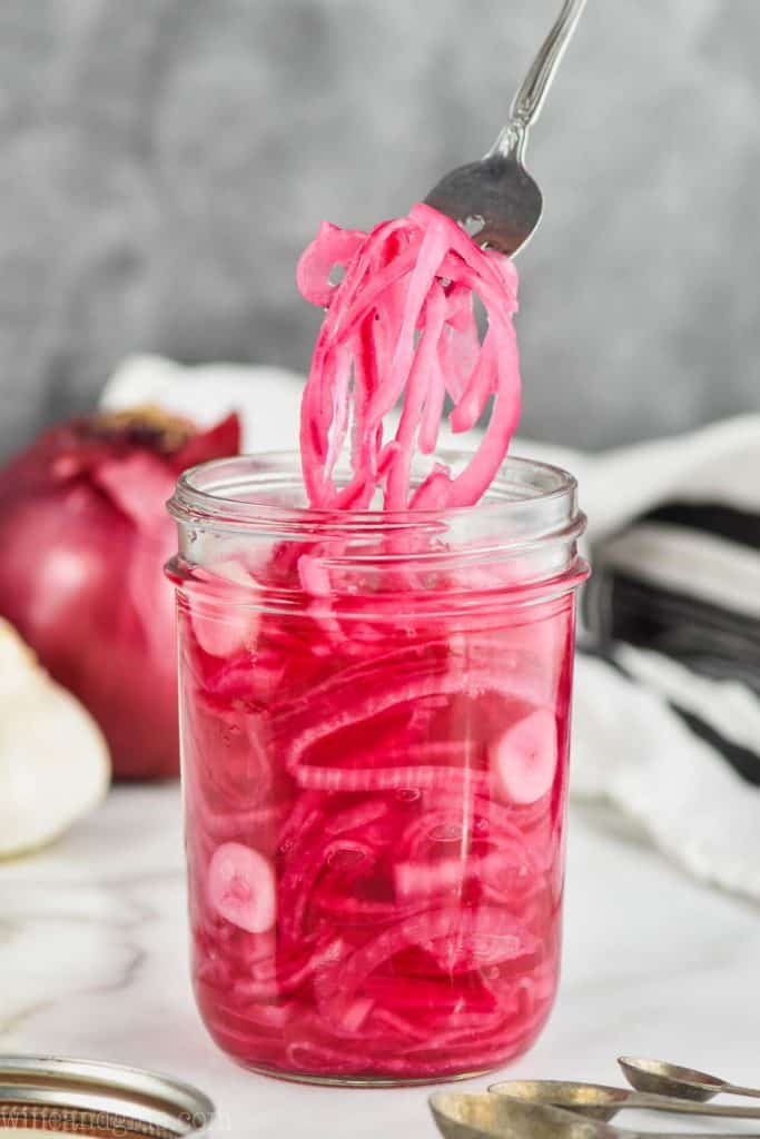 quick pickled red onions being pulled from a canning jar